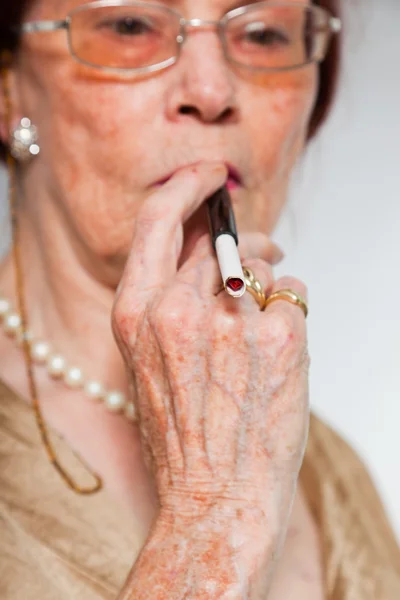 Retrato de una mujer mayor guapa usando gafas con cara expresiva mostrando emociones. Fumar un cigarrillo. Actuando joven. Estudio plano aislado sobre fondo gris . —  Fotos de Stock