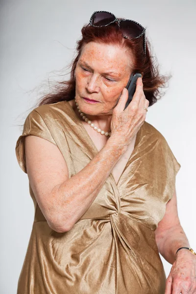 Retrato de una mujer mayor de buen aspecto con cara expresiva mostrando emociones. Llamando con el teléfono celular. Actuando joven. Estudio plano aislado sobre fondo gris . — Foto de Stock