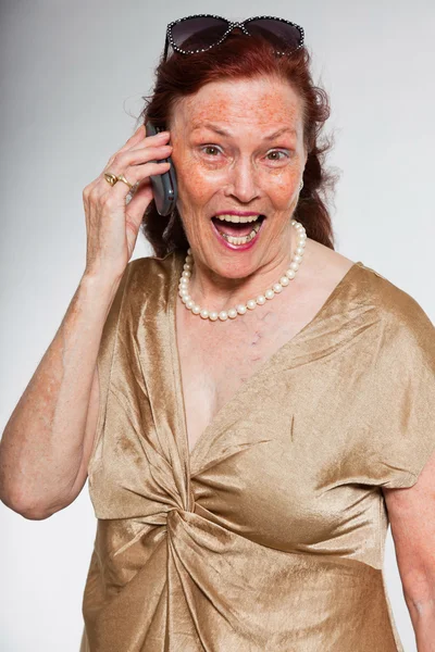 Portret van goed uitziende senior vrouw met expressief gezicht toont emoties. bellen met mobiele telefoon. handelend jonge. studio opname geïsoleerd op grijze achtergrond. — Stockfoto