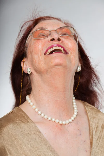 Retrato de una mujer mayor guapa usando gafas con cara expresiva mostrando emociones. Feliz y libre. Actuando joven. Estudio plano aislado sobre fondo gris . —  Fotos de Stock