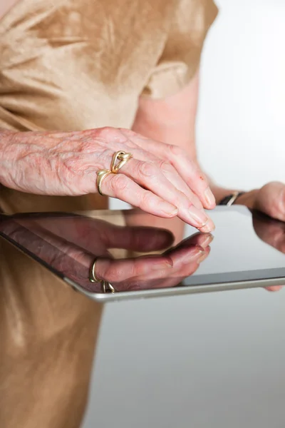 Mãos de uma mulher idosa usando um tablet. Estúdio filmado em fundo cinza . — Fotografia de Stock