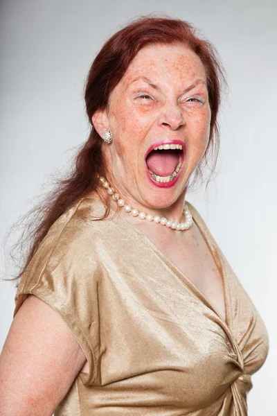 Portrait of good looking senior woman with expressive face showing emotions. Screaming. Acting young. Studio shot isolated on grey background. — Stock Photo, Image