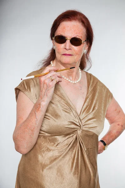 Retrato de una mujer mayor de buen aspecto con cara expresiva mostrando emociones. Usando gafas de sol y fumando un cigarrillo. Actuando joven. Estudio plano aislado sobre fondo gris . — Foto de Stock