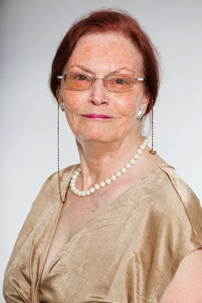 Портрет добродушної старшої жінки в окулярах з виразним обличчям, що демонструє емоції. Посміхаючись. Поводитися молодо. Студійний знімок ізольовано на сірому фоні . — стокове фото