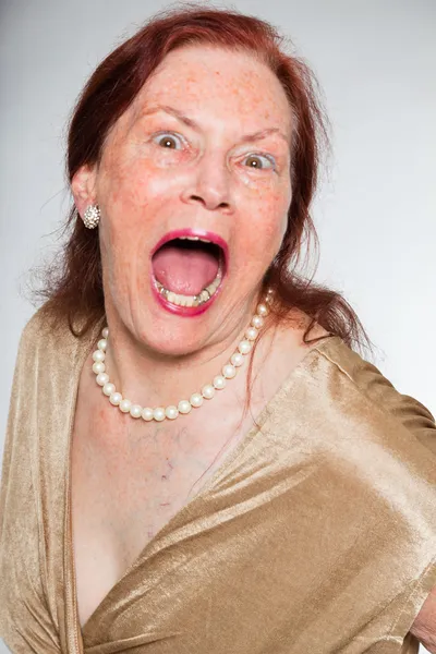 Portrait of good looking senior woman with expressive face showing emotions. Screaming. Acting young. Studio shot isolated on grey background. — Stock Photo, Image