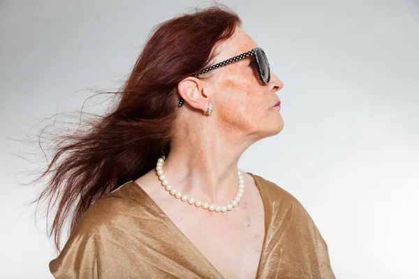 Porträtt av bra senior kvinna bär solglasögon med uttrycksfulla ansikte visar känslor. glad och fri. agerar unga. Studio skott isolerade på grå bakgrund. — Stockfoto