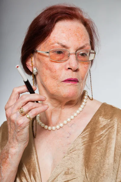 Porträtt av bra senior kvinna bär glasögon med uttrycksfulla ansikte visar känslor. röka en cigarett. agerar unga. Studio skott isolerade på grå bakgrund. — Stockfoto