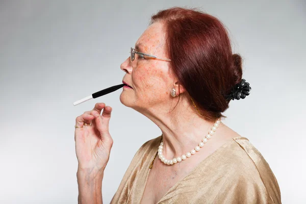 Retrato de boa aparência mulher idosa vestindo óculos com rosto expressivo mostrando emoções. Fumar um cigarro. A agir jovem. Estúdio tiro isolado em fundo cinza . — Fotografia de Stock