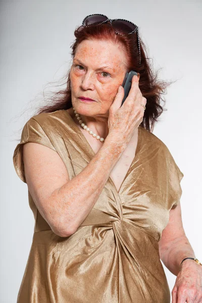 Portrait of good looking senior woman with expressive face showing emotions. Calling with cell phone. Acting young. Studio shot isolated on grey background. — Stock Photo, Image