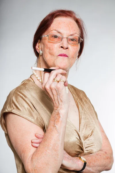 Porträt einer gut aussehenden Seniorin mit Brille und ausdrucksstarkem Gesicht, die Emotionen zeigt. Zigarette rauchen. Jung handeln. Studioaufnahme isoliert auf grauem Hintergrund. — Stockfoto