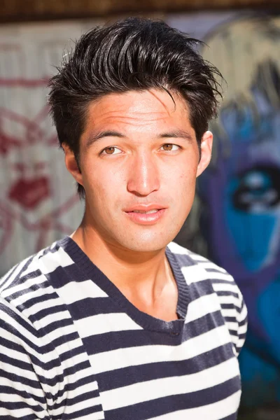 Urban asiatiska mannen. Snygg. cool kille. klädd i blå vit randig tröja. stående framför trävägg med graffiti. — Stockfoto