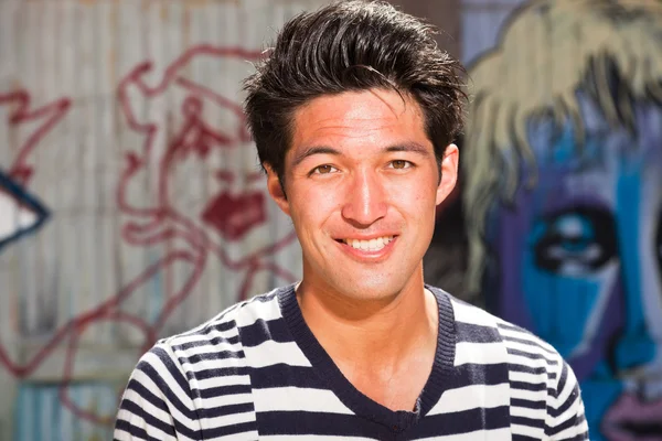 Homme asiatique urbain. Beau look. Cool mec. Portant un pull rayé bleu blanc. Debout devant un mur en bois avec des graffitis . — Photo
