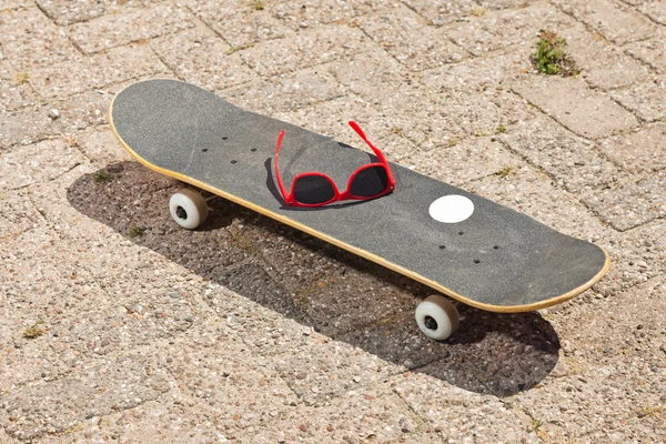 Pro skateboard with red sunglasses on it on the street. — Stock Photo, Image