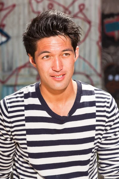 Städtischer asiatischer Mann. gut aussehend. Cooler Typ. trägt einen blau-weiß gestreiften Pullover. vor Holzwand mit Graffiti. — Stockfoto
