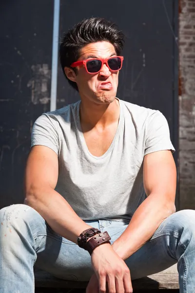 Urbaner asiatischer Mann mit roter Sonnenbrille, der ein lustiges Gesicht macht. gut aussehend. Cooler Typ. trägt graues Hemd und Jeans. — Stockfoto