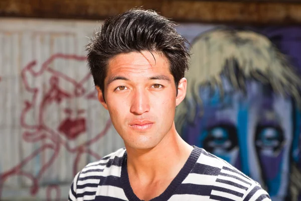 Hombre asiático urbano. Muy guapo. Un tipo genial. Usando jersey azul a rayas blancas. De pie frente a la pared de madera con graffiti . —  Fotos de Stock