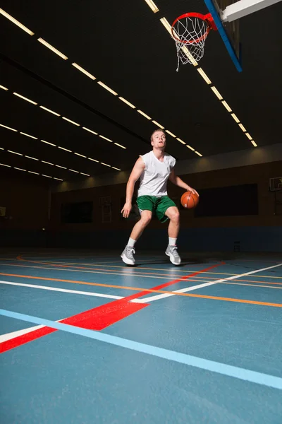 Taai gezonde jonge man spelen basketbal in sportschool binnen. dragen witte overhemd en groene shorts. — Stockfoto