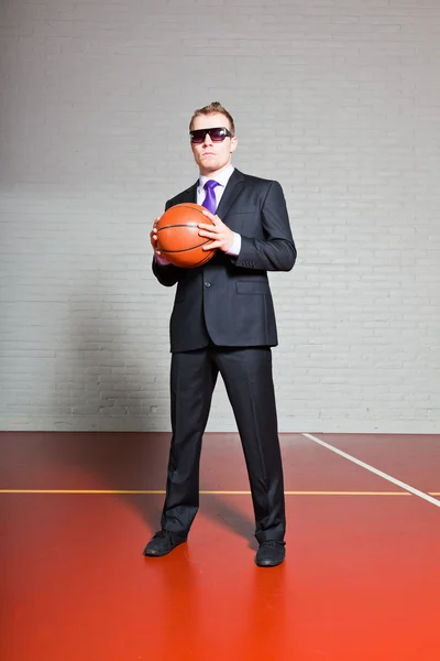 Pebisnis dengan bola basket. Mengenakan kacamata hitam. Pemuda tampan dengan rambut pirang pendek. Gym indoor . — Stok Foto