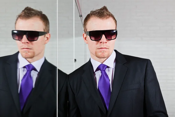 Freddo uomo d'affari di bell'aspetto con occhiali da sole scuri in piedi contro lo specchio . — Foto Stock