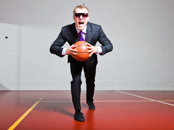 Angry business man with basketball. Wearing dark sunglasses. Good looking young man with short blond hair. Gym indoor. — Stock Photo, Image