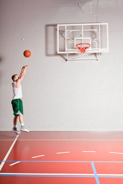 坚强健康的年轻人在健身房室内打篮球。身穿白衬衫和绿色短裤. — 图库照片