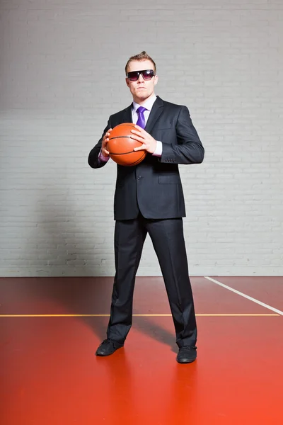 Pebisnis dengan bola basket. Mengenakan kacamata hitam. Pemuda tampan dengan rambut pirang pendek. Gym indoor . — Stok Foto