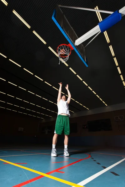 Dur jeune homme en bonne santé jouant au basket-ball en salle de gym. Porter une chemise blanche et un short vert . — Photo