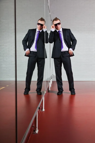 Pria bisnis tampan dengan kacamata hitam berdiri melawan cermin di gym . — Stok Foto