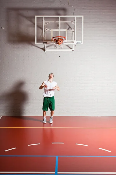 Duro joven saludable jugando baloncesto en el gimnasio interior. Vestir camisa blanca y pantalones cortos verdes . —  Fotos de Stock