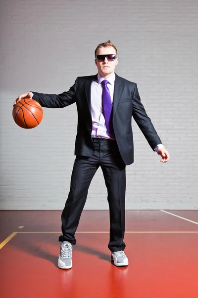 Ο άνθρωπος των επιχειρήσεων με το μπάσκετ. φοράει σκούρα γυαλιά ηλίου. όμορφος νεαρός άνδρας με κοντά ξανθά μαλλιά. γυμναστήριο, εσωτερική. — Φωτογραφία Αρχείου