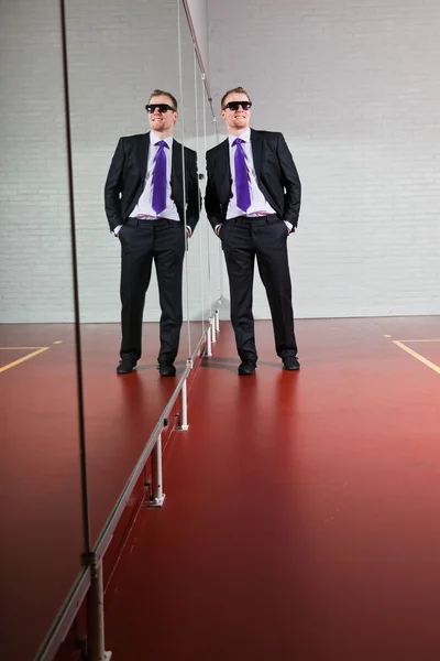 クールな良い探しビジネスの男性とジムでミラーに対して立っている濃いサングラス. — ストック写真