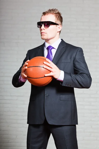 Uomo d'affari con pallacanestro. Indossava occhiali da sole scuri. Bel giovanotto con i capelli biondi corti. Muro di mattoni bianchi . — Foto Stock