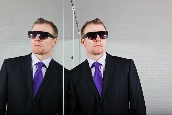 Cool good looking business man with dark sunglasses standing against mirror. — Stock Photo, Image
