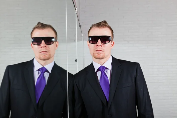 Pria bisnis tampan dengan kacamata hitam berdiri melawan cermin . — Stok Foto
