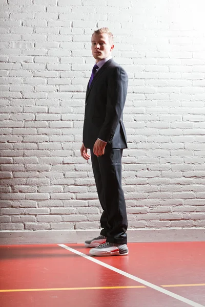 Симпатичный молодой человек с короткими светлыми волосами в темном костюме и баскетбольной обуви. Тренажерный зал . — стоковое фото