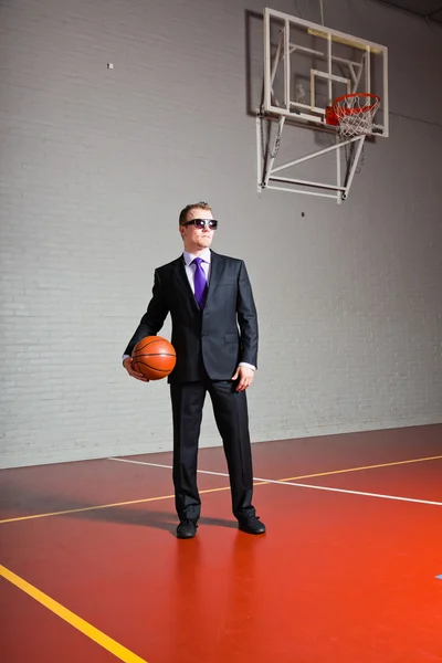 Hombre de negocios con baloncesto. Llevando gafas de sol oscuras. Joven guapo con el pelo corto y rubio. Gimnasio interior . —  Fotos de Stock