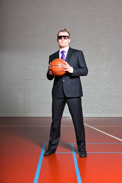 Hombre de negocios con baloncesto. Llevando gafas de sol oscuras. Joven guapo con el pelo corto y rubio. Gimnasio interior . — Foto de Stock