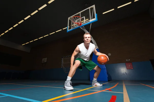 Taai gezonde jonge man spelen basketbal in sportschool binnen. dragen witte overhemd en groene shorts. — Stockfoto