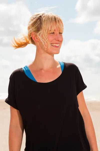 Mulher loira bonita feliz na praia. Desfrutando da natureza. Céu azul nublado. Vestindo camisola preta . — Fotografia de Stock