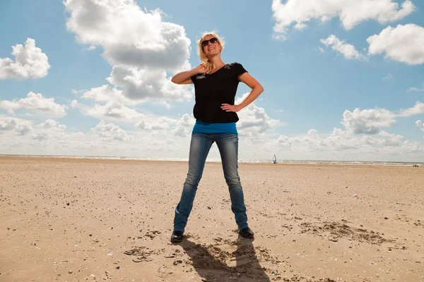 Šťastný pěkné blond žena na pláži. užívat přírodu. modré oblohy jasno. nosí černý svetr a sluneční brýle. — Stock fotografie