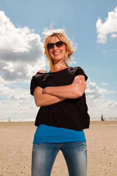 Felice bella donna bionda sulla spiaggia. Godersi la natura. Cielo blu nuvoloso. Indossare maglione nero e occhiali da sole . — Foto Stock