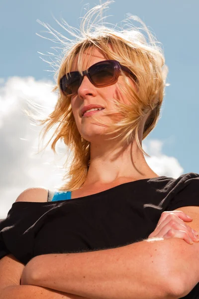 हैप्पी सुंदर सुनहरे बालों वाली महिला समुद्र तट पर प्रकृति का आनंद लेना। नीला बादल वाला आकाश। काले स्वेटर और धूप का चश्मा पहनना . — स्टॉक फ़ोटो, इमेज