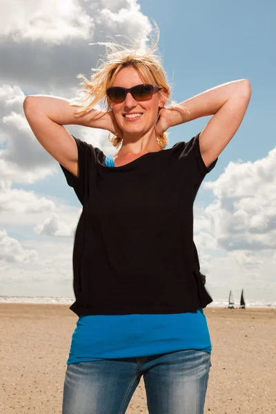 Felice bella donna bionda sulla spiaggia. Godersi la natura. Cielo blu nuvoloso. Indossare maglione nero e occhiali da sole . — Foto Stock