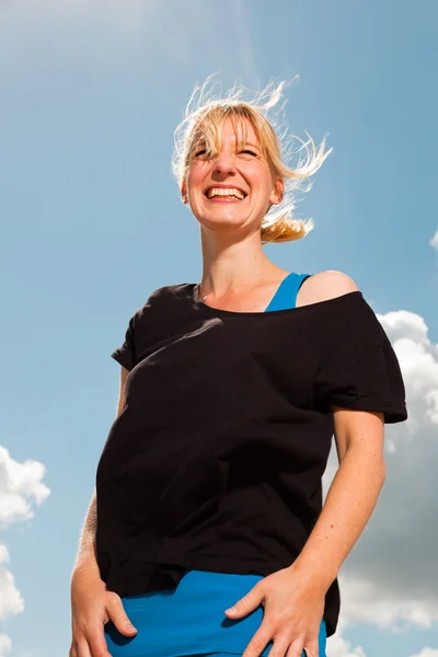 Gelukkig vrij blonde vrouw op het strand. genieten van de natuur. blauwe bewolkte hemel. zwarte trui dragen. — Stockfoto