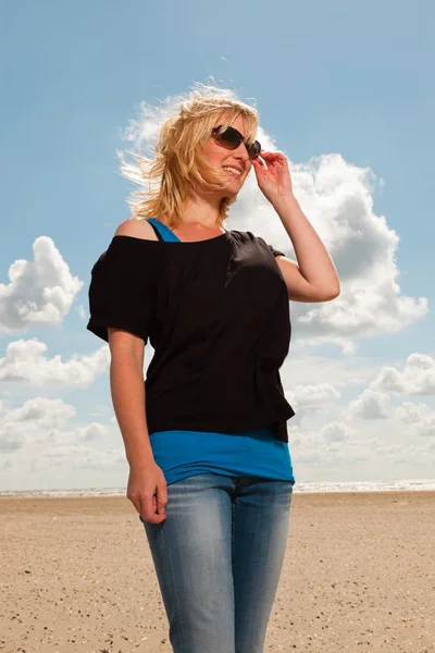 Jolie jolie femme blonde sur la plage. Profiter de la nature. Ciel nuageux bleu. Porter un pull noir et des lunettes de soleil . — Photo