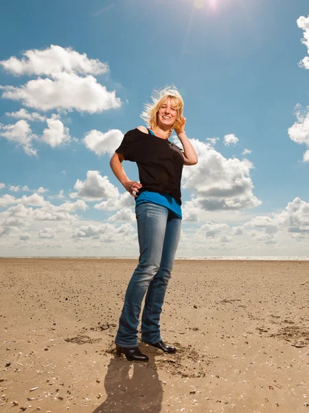 Lykkelig blond dame på stranda. Nyter naturen. Blå skyet himmel. Svart genser . – stockfoto