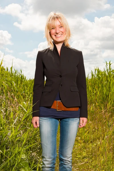Happy pretty young blond woman enjoying nature. Field with high grass. Blue cloudy sky. Black jacket. — Stock Photo, Image