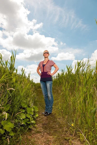 Zadowolony ładny blond kobieta z okulary z przyrodą. pole z wysokiej trawy. błękitne niebo pochmurne. ubrany w czerwony. — Zdjęcie stockowe