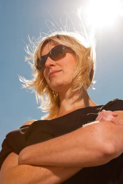 Mulher loira bonita feliz na praia. Desfrutando da natureza. Céu azul nublado. Vestindo camisola preta e óculos escuros . — Fotografia de Stock