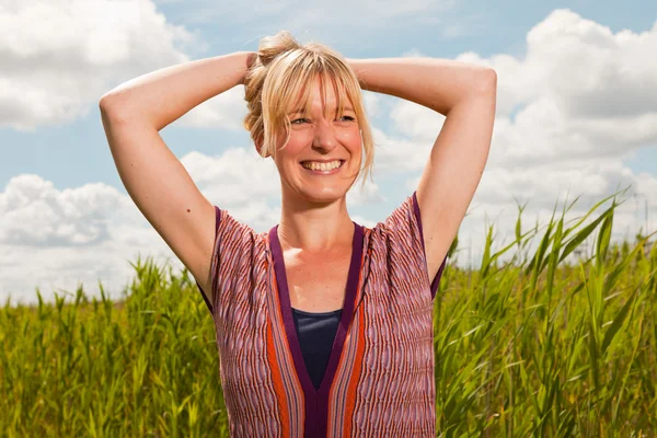 Joyeux jeune femme blonde appréciant la nature. Champ avec herbe haute. Ciel nuageux bleu. Habillé en rouge . — Photo